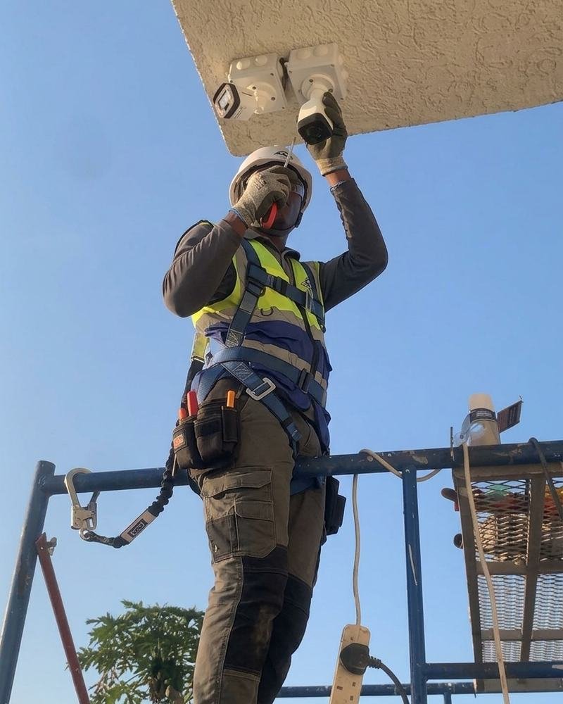 A technician in a safety harness installing cameras from scaffolding